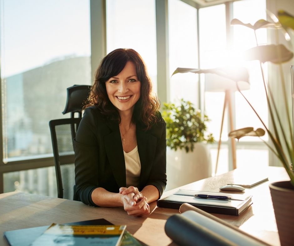 Female productive project managers sitting at her desk in her office and smiling confidently